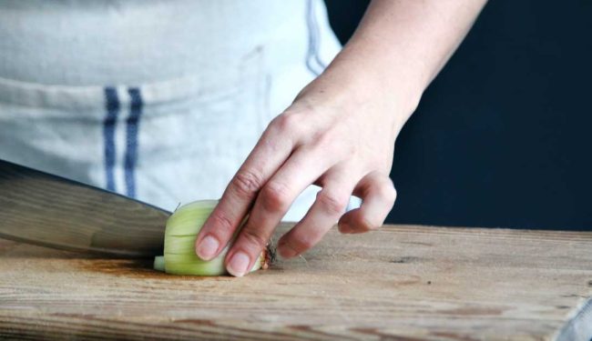 A person wearing an apron cuts an onion on a cutting board with a chef's knife.