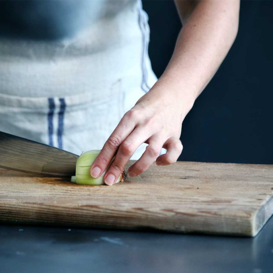 A person wearing an apron cuts an onion on a cutting board with a chef's knife.