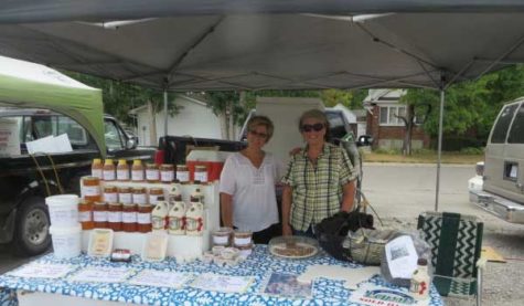 Two people stand inside a booth at a Farmers' market