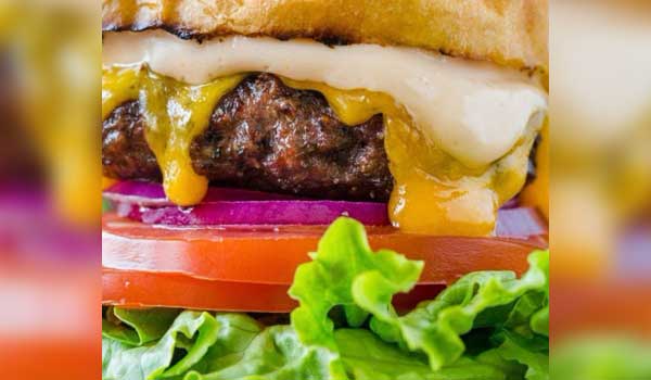 Close-up of a burger with onions, tomatoes, cheese, and lettuce