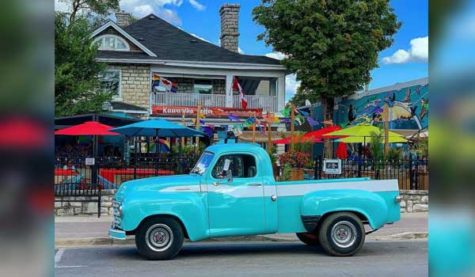 A retro blue pickup truck is parked in front of a building with a patio.