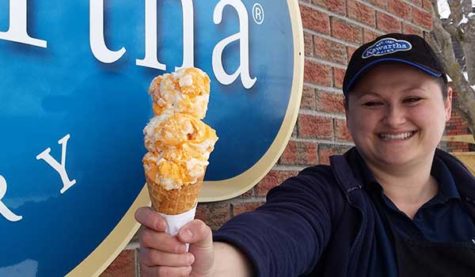 A person holds an ice cream cone with three scoops of orange ice cream