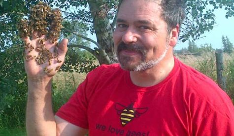 A smiling person holds his bee-covered hand up in the air.