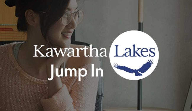 A smiling person sits at her computer. On top of the image is the Kawartha Lakes Jump In logo.