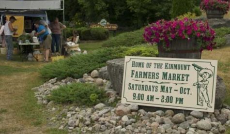 A sign sits at the entrance to a farmers' market. The sign says "Home of the Kinmount Farmers' Market"